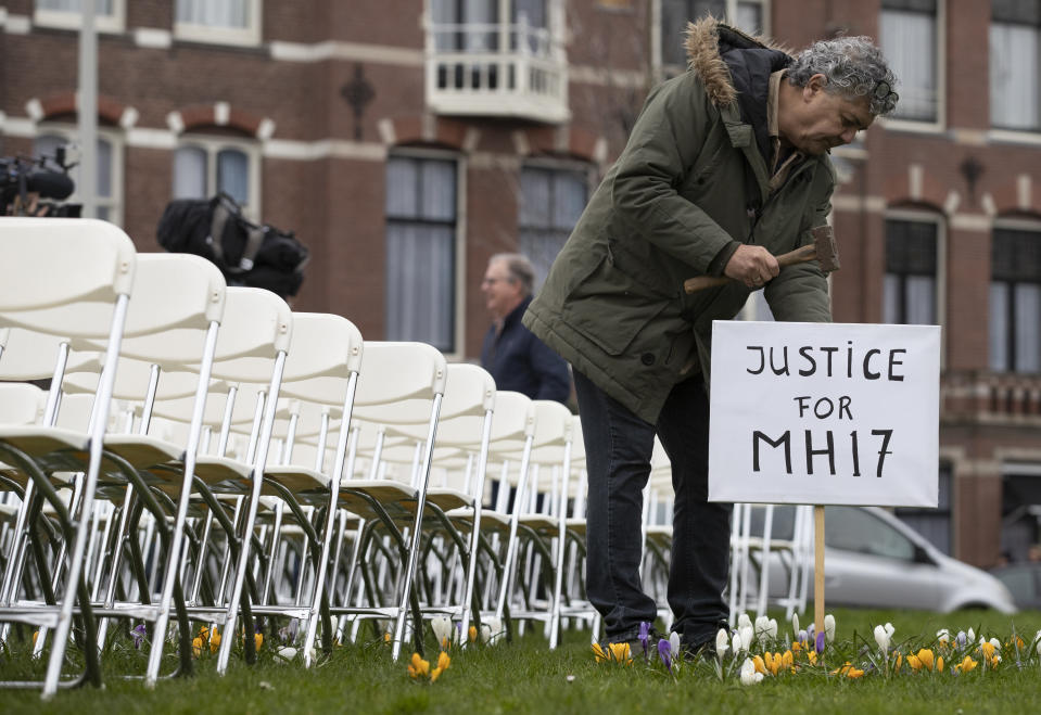 FILE- In this Sunday, March 8, 2020, file photo Rob Fredriksz, who lost his son Bryce and his girlfriend Daisy, places a sign next to 298 empty chairs, each chair for one of the 298 victims of the downed Malaysia Air flight MH17, in a park opposite the Russian embassy in The Hague, Netherlands. The trial in absentia in a Dutch courtroom of three Russians and a Ukrainian charged in the downing of Malaysia Airlines flight MH17 in 2014 moves to the merits phase, when judges and lawyers begin assessing evidence. (AP Photo/Peter Dejong, File)