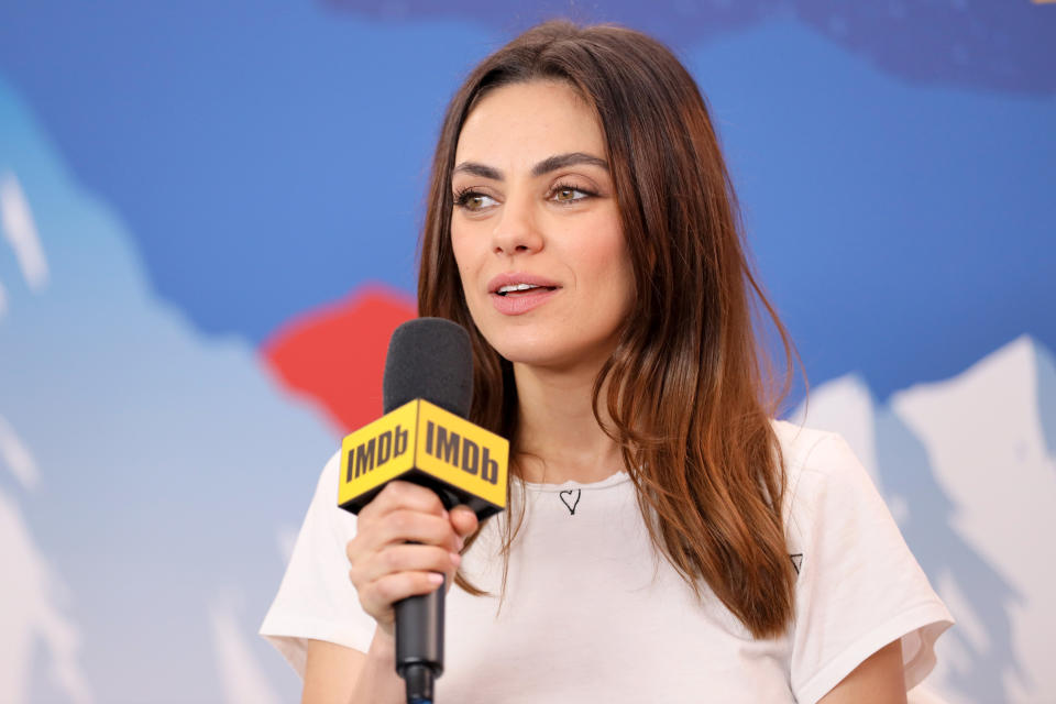 Photo of Mila Kunis in a white t-shirt holding an IMDb-branded microphone