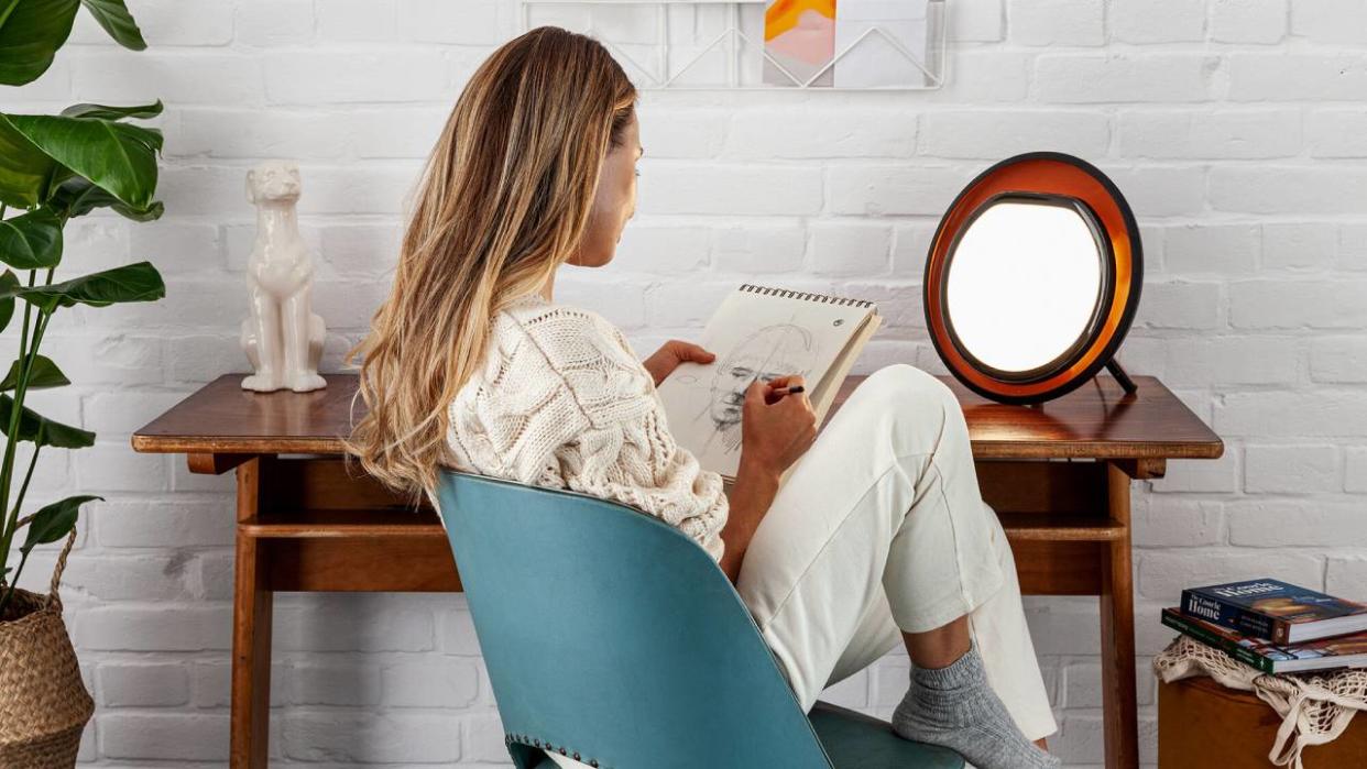  Woman sitting in front of a Lumie SAD lamp while drawing. 