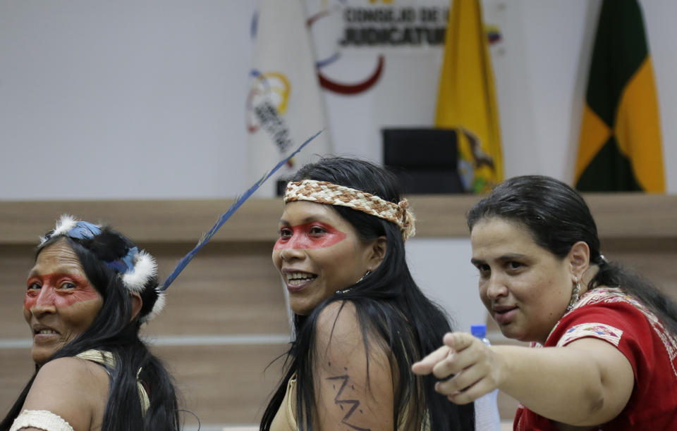 Waoranis leader Nemonte Nenquimo, center, and lawyer Lina Espinosa, right, wait for the start of a hearing on a lawsuit filed by the Waoranis against the Ministry of Non-Renewable Natural Resources for opening up oil concessions on their ancestral land, in Puyo, Ecuador, Friday, April 26, 2019. The judge went on to rule in favor of the Waoranis. (AP Photo/Dolores Ochoa)
