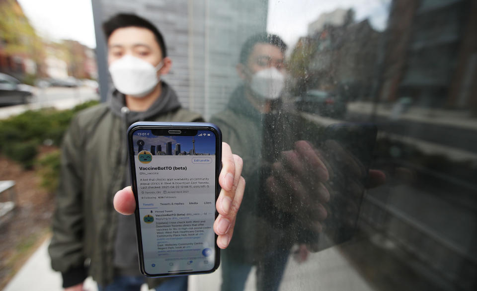 Software developer wearing a mask holds out a smartphone with showing his Twitter bot on the screen.