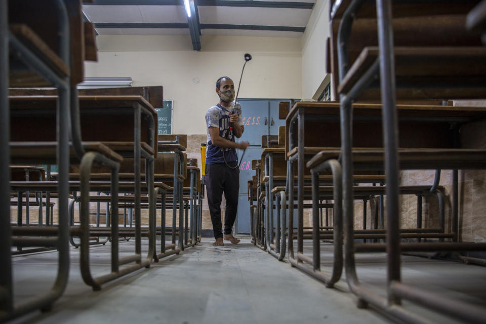 A man sanitizes a classroom ahead of the partial reopening of schools in New Delhi, India, Tuesday, Aug. 31, 2021. Many students in India will be able to step inside a classroom for the first time in nearly 18 months from Wednesday, as authorities have given the green light to partially reopen schools despite apprehension from some parents and signs that coronavirus infections are picking up again. Schools and colleges in least six states will reopen in a gradual manner with health measures in place throughout September. In New Delhi, all staff must be vaccinated and class sizes will be capped at 50% with staggered seating and sanitized desks. (AP Photo/Altaf Qadri)