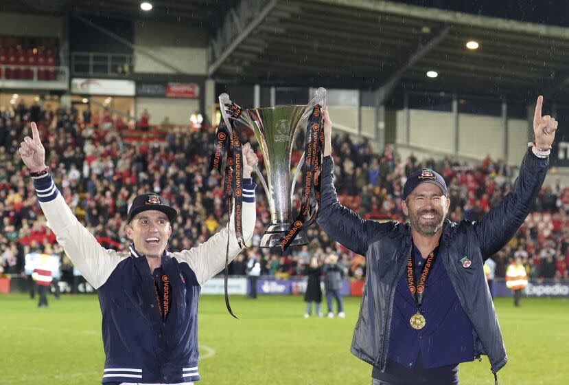 Wrexham co-owners Rob McElhenney, left, and Ryan Reynolds celebrates with the trophy after their team clinched promotion following the National League soccer match between Wrexham and Boreham Wood at The Racecourse Ground, in Wrexham, Wales, Saturday April 22, 2023. (Martin Rickett/PA via AP)
