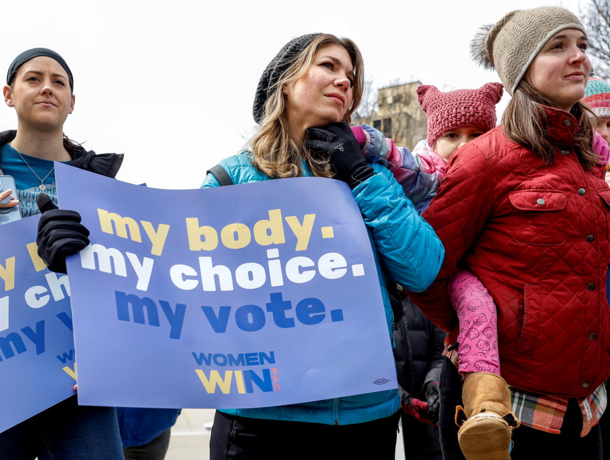 Romy Stokes, 5, in pink pants and wool hat with ears, clings to her mother, as another protester holds a sign saying: my body. my choice. my vote. Women win! 