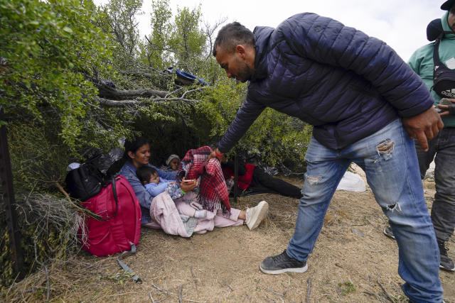 A migrant from Colombia, right, gives a blanket to a Colombian woman with small children as the group waits to apply for asylum after crossing the border Wednesday, May 10, 2023, near Jacumba, Calif. The group have been camping just across the border for days, waiting to apply for asylum in the United States. As members of the group get to the front of the line to be escorted into vans, they hand off all warm clothing to those who might still have to camp overnight. (AP Photo/Gregory Bull)