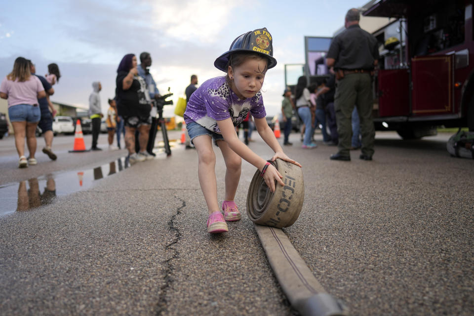 Cali King, 7, rolls up a fire hose while attending a National Night Out event with her family in the Colony Ridge development Tuesday, Oct. 3, 2023, in Cleveland, Texas. The booming Texas neighborhood is fighting back after Republican leaders took up unsubstantiated claims that it has become a magnet for immigrants living in the U.S. illegally and that cartels control pockets of the neighborhood. (AP Photo/David J. Phillip)