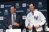 FILE - In this Dec. 18, 2019, file photo, New York Yankees manager Aaron Boone, left, smiles as Gerrit Cole tries on a Yankee jersey as he is introduced in New York. The pitcher agreed to a 9-year $324 million contract. "He's going to be a game changer for us," Yankees owner Hal Steinbrenner said. "The city's buzzing, and it's continued since the day we signed him." (AP Photo/Mark Lennihan, File)