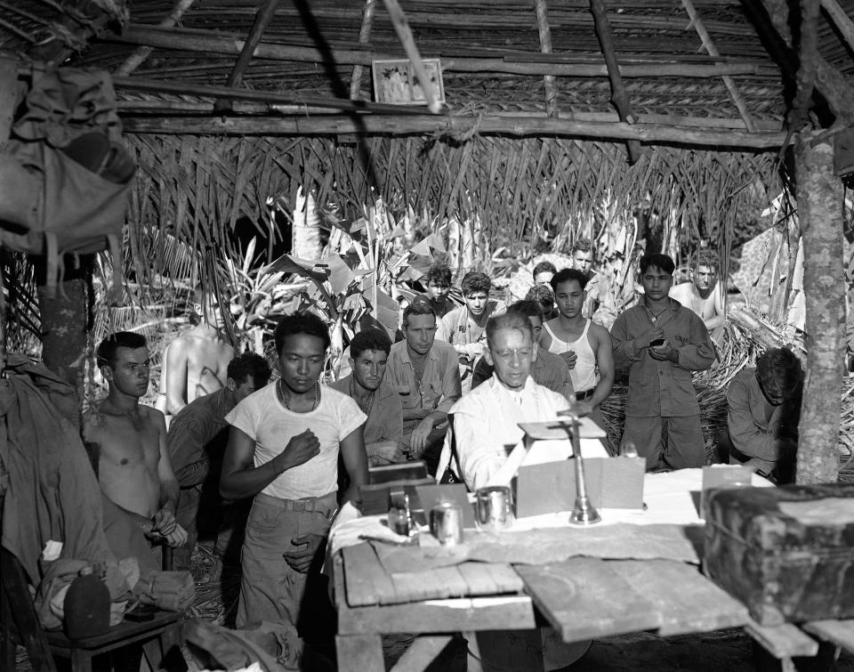 FILE - This Nov. 1, 1944 file photo shows the first religious service on Guam after U.S. landings are attended by soldiers, Nov. 1, 1944. An indigenous Chamorro serves as altar boy in this improvised hut. The 1941 Japanese invasion of Guam, which happened on the same December day as the attack on Hawaii's Pearl Harbor, set off years of forced labor, internment, torture, rape and beheadings. More than 75 years later, thousands of people on Guam, a U.S. territory, are expecting to get long-awaited compensation for their suffering at the hands of imperial Japan during World War II. (AP Photo/Joe Rosenthal, File)