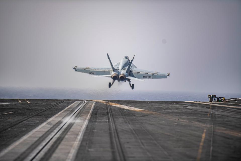 A fighter jet takes off from the flight deck of an aircraft carrier at sea.