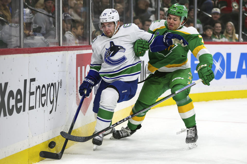 Vancouver Canucks left wing Nils Hoglander, left, and Minnesota Wild defenseman Brock Faber (7) compete for the puck during the first period of an NHL hockey game Saturday, Dec. 16, 2023, in St Paul, Minn. (AP Photo/Matt Krohn)