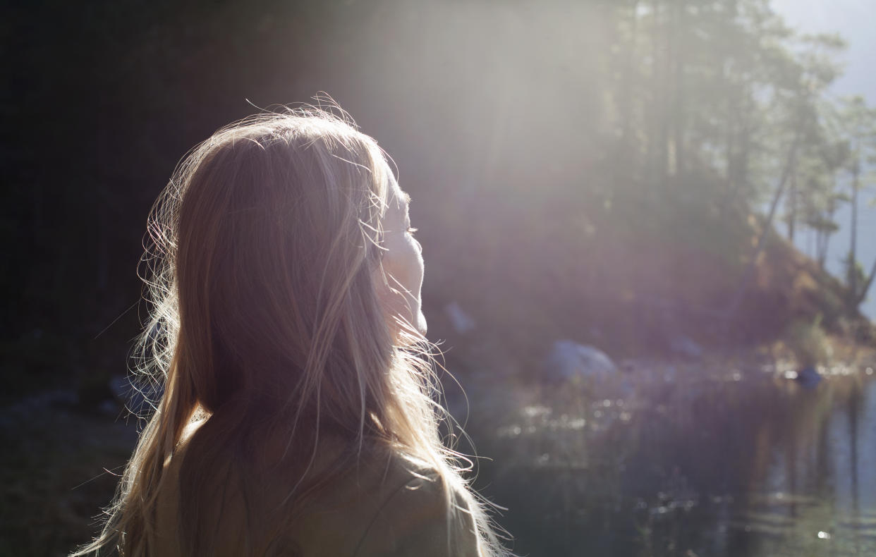 Frau steht draußen und lässt sich die Sonne ins Gesicht scheinen