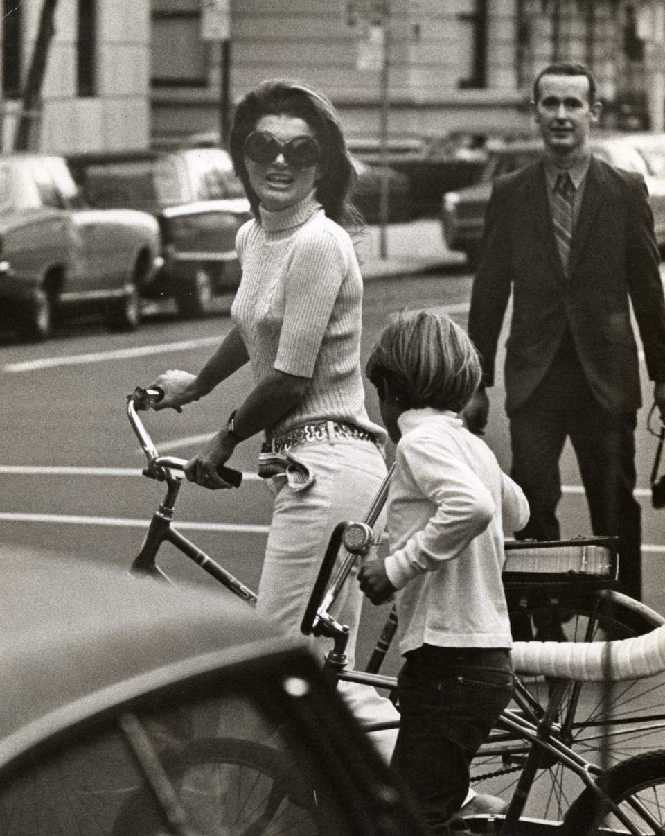 <p>Wearing a knit turtleneck and belted white jeans, Jackie and John Jr. take a bike ride in New York City. <br></p>