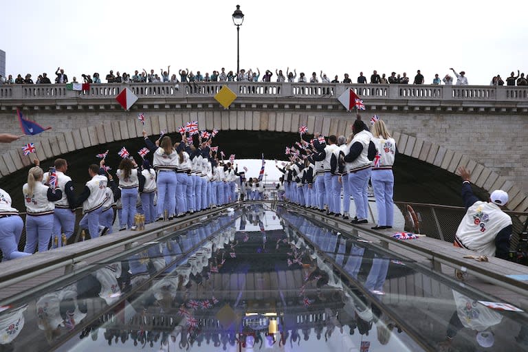 Los espectadores aplauden mientras los atletas de Gran Bretaña pasan bajo un puente a lo largo del río Sena