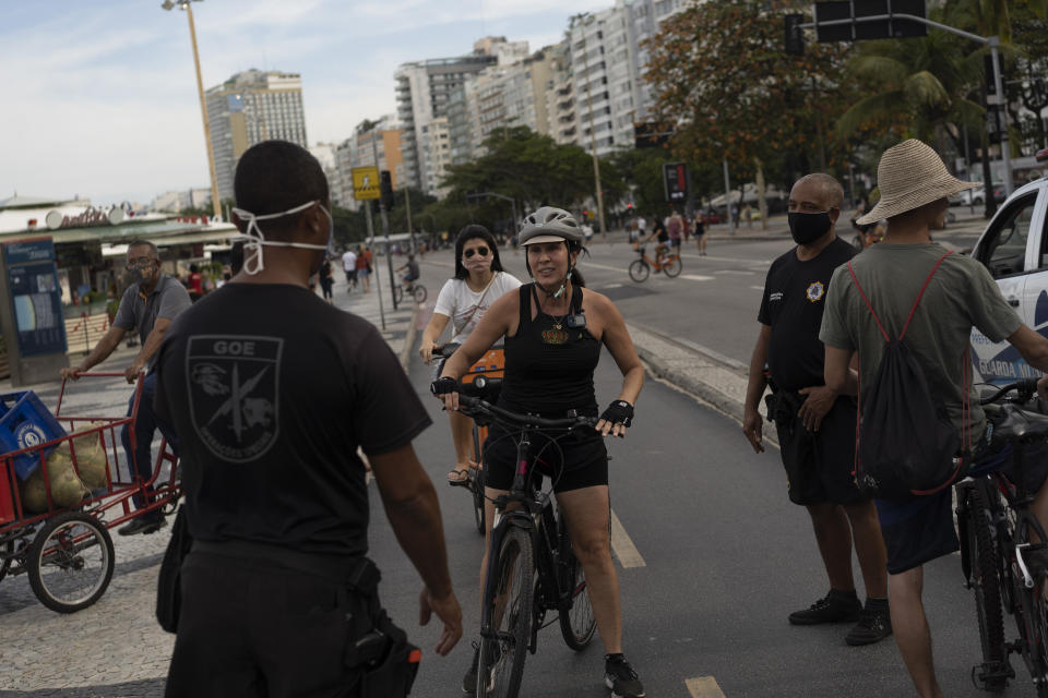 A municipal guard stops a woman on a bike to tell her to wear a mask at Copacabana beach amid the outbreak of the new coronavirus in Rio de Janeiro, Brazil, Sunday, July 12, 2020. (AP Photo/Leo Correa)