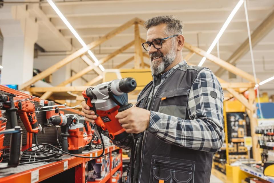 Smiling person holding a drill in a tool shop. 