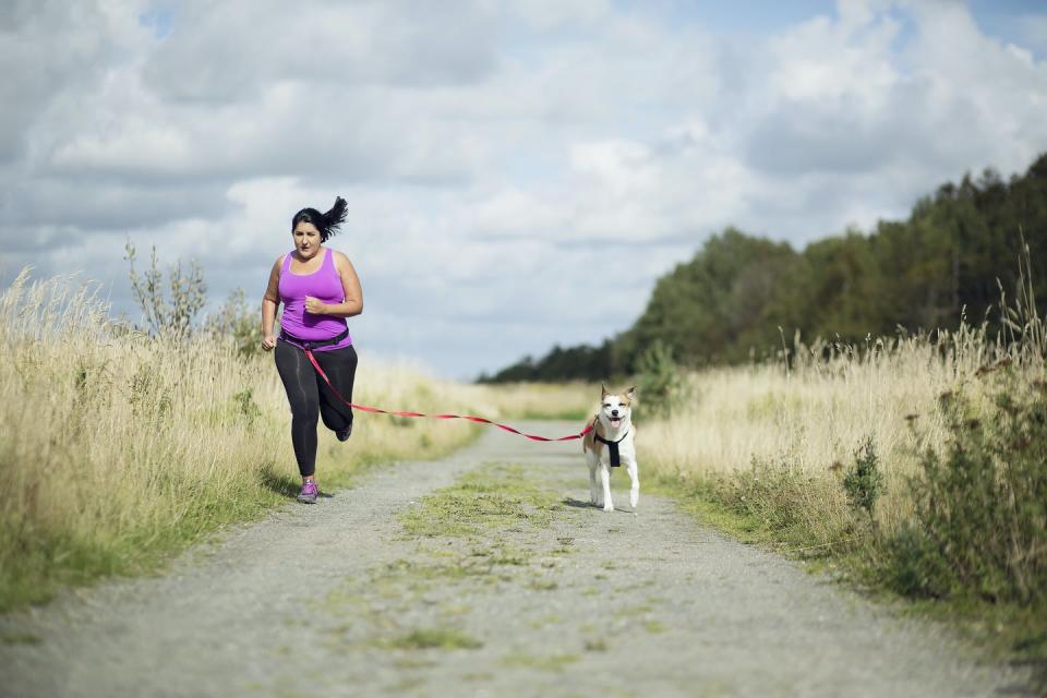 Woman running with dog on a beach road.