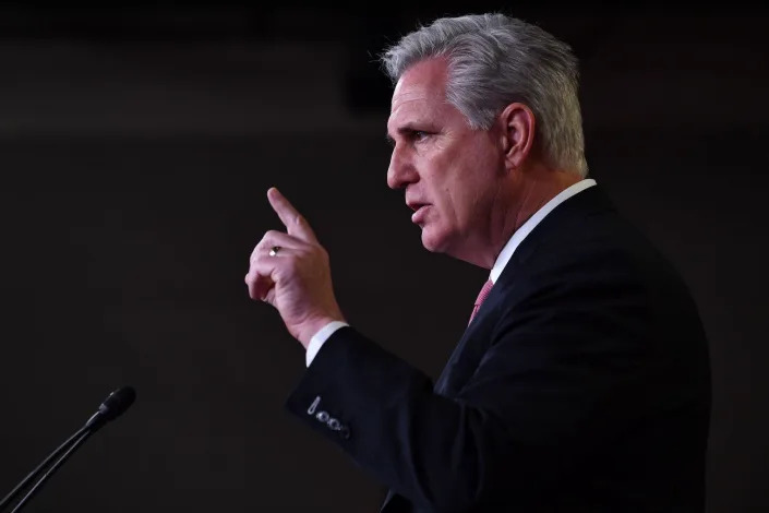 House Minority Leader Kevin McCarthy, his left index finger pointed skyward, addresses reporters from a stage during a Capitol Hill press conference.