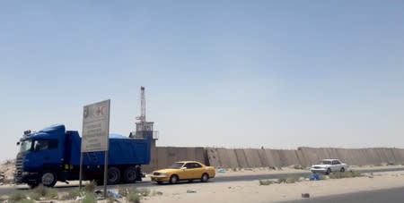 Vehicles drive past next to a security barrier of Zubair oilfield after a rocket landed at a residential and operations headquarters of several oil companies, at Burjesia area in Basra