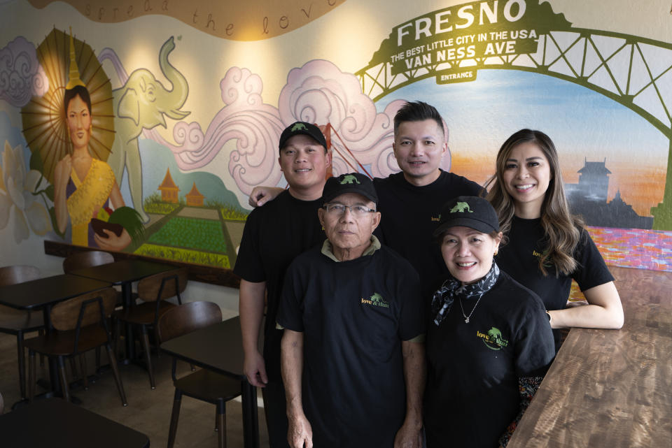 Owner David Rasavong, center, joined by his family, his wife Anna Le Nguyen, right and his cousin Tito Thepkaysone, left and his mother Bounma Rasavong along with his father Minh Rasavong Oriyavong a family run resturant "Love & Thai" in Fresno, Calif. on Wednesday, Dec. 20, 2023. They proudly stand in front of a mural depicting the family's journey from Laos to San Francisco then to Fresno. (AP Photo/Richard Vogel)