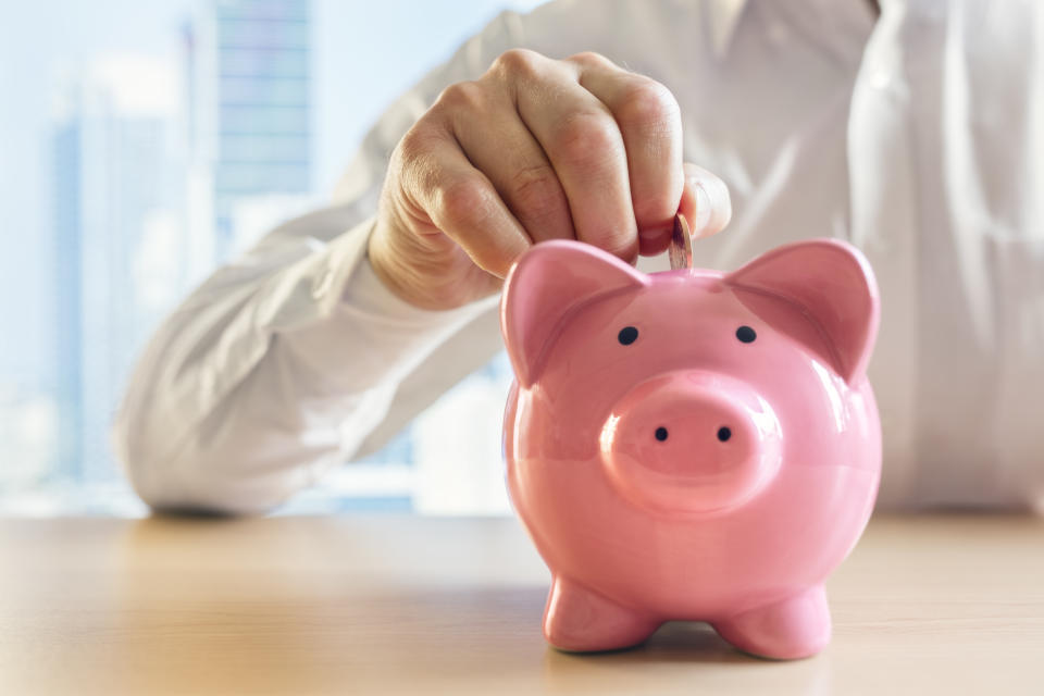 Man putting a coin into a pink piggy bank concept for savings and finance