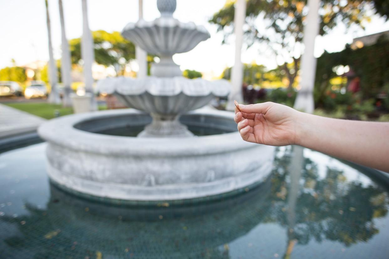 tourist holding out a penny to make a wish when throwing it into a public fountain in a mall plaza on the island of Hawaii