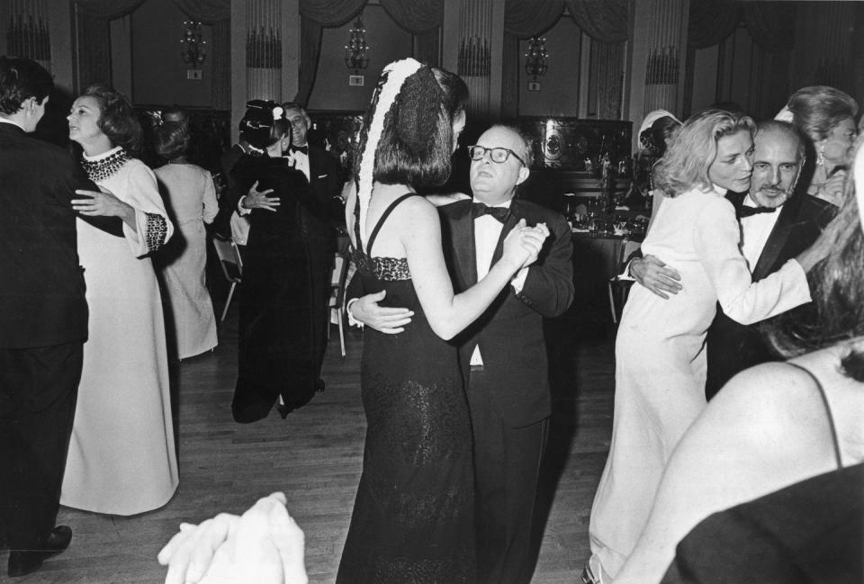 truman capote dances with a woman as they are surrounded by other couples dancing, everyone wears formal attire in the ballroom
