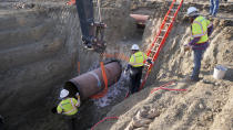 This April 13, 2020 photo provided by TC Energy shows workers for TC Energy installing a section of the Keystone XL crude oil pipeline at the U.S.-Canada border north of Glasgow, Mont. Two people working on the Keystone XL oil pipeline have tested positive for the coronavirus in northern Montana, but the company said Thursday, Aug. 8, 2020, that construction work on the disputed project will continue after a temporary shut down of a pipe storage yard. (TC Energy via AP)