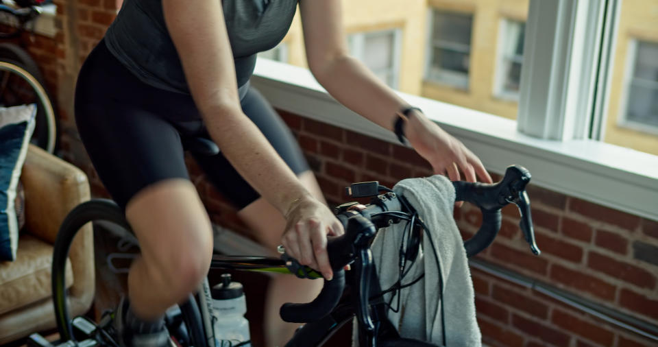 A caucasian woman in her 30s works out on a bike trainer in an urban apartment.