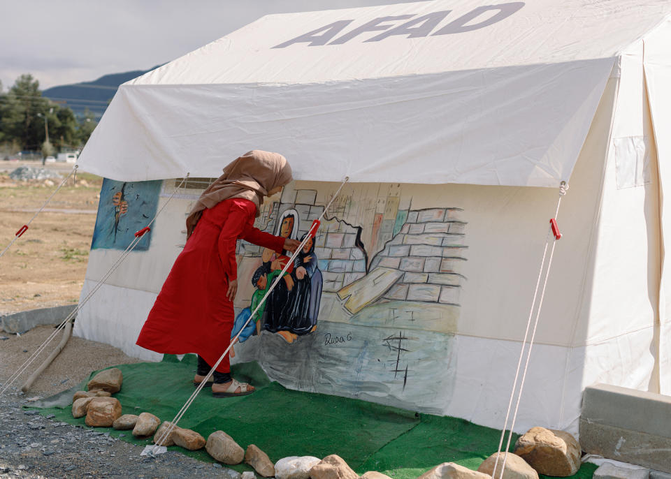 A neighbour interacts with Duah Gawi’s paintings, inspired by real-life scenarios witnessed the days following the earthquake inside the informal tent settlement where Gawi has been living following the destruction of their home in Islahiye, Gaziantep, in April. Despite the freedom of movement granted by the Turkish government to Syrian refugees after the earthquake, Gawi's family doesn't have relatives living outside the affected area and was unable to benefit.<span class="copyright">Carola Cappellari</span>