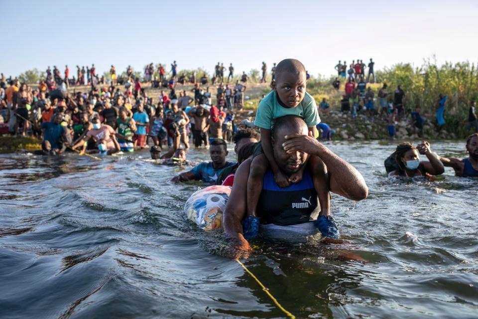 A man shields his face as he crosses the Rio Grande with a youngster on his shoulders