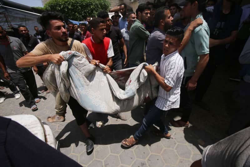 Palestinian men carry the body of a dead person at Al-Aqsa Martyrs Hospital following simultaneous Israeli attacks on Nuseirat Refugee Camp, al-Bureij Refugee Camp and al-Maghazi Refugee Camp. Israeli special forces rescued four hostages in broad daylight on Saturday from the Nuseirat refugee district in the centre of the Gaza Strip after 246 days in captivity, the army said. Omar Naaman/dpa