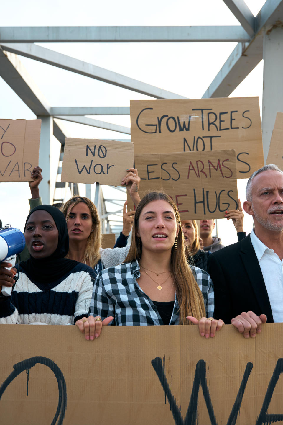 Group of protesters holding signs with anti-war messages like "Grow Trees Not Arms" and "No War."