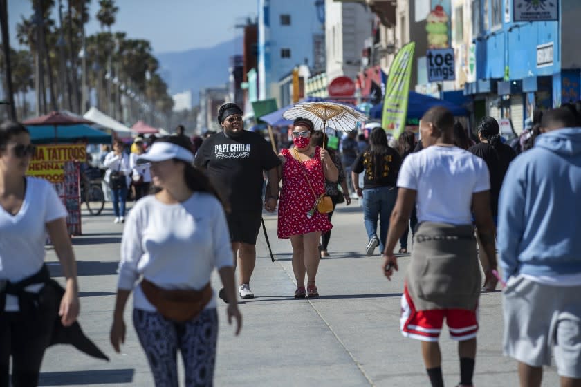 VENICE BEACH, CA - MARCH 29, 2021: Eddie Gonzalez, 30, and Barbara Sanchez, 32, visiting from Santa Cruz, enjoy a walk with others on the boardwalk at Venice Beach on a sunny, Monday afternoon. (Mel Melcon / Los Angeles Times)