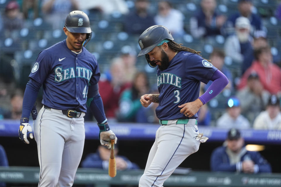 Seattle Mariners' J.P. Crawford (3) scores on a wild pitch as Julio Rodríguez, left, looks on in the second inning of the second game of a baseball doubleheader against the Colorado Rockies Sunday, April 21, 2024, in Denver. (AP Photo/David Zalubowski)