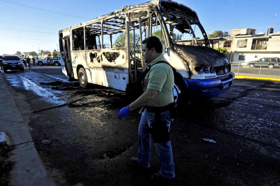 A forensic specialist walks around a burned bus in the town of Zapopan, Mexico, Thursday, Jan. 30, 2014. The bus was torched by unidentified attackers while officials detained the son of an alleged leader of a drug cartel during a raid in this town. A federal official who was not authorized to be quoted by name says the man detained is Ruben Oseguera. His father Nemesio Oseguera allegedly leads the Jalisco New Generation cartel. (AP Photo)