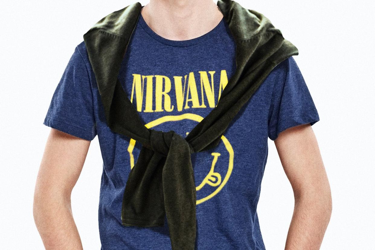 A torso wearing a blue Nirvana smiley face shirt with a sweater tied preppily around the shoulders.