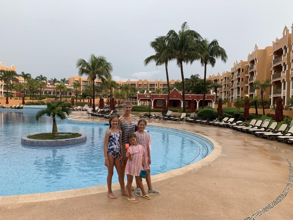 A woman and her three children standing in front of a resort pool.