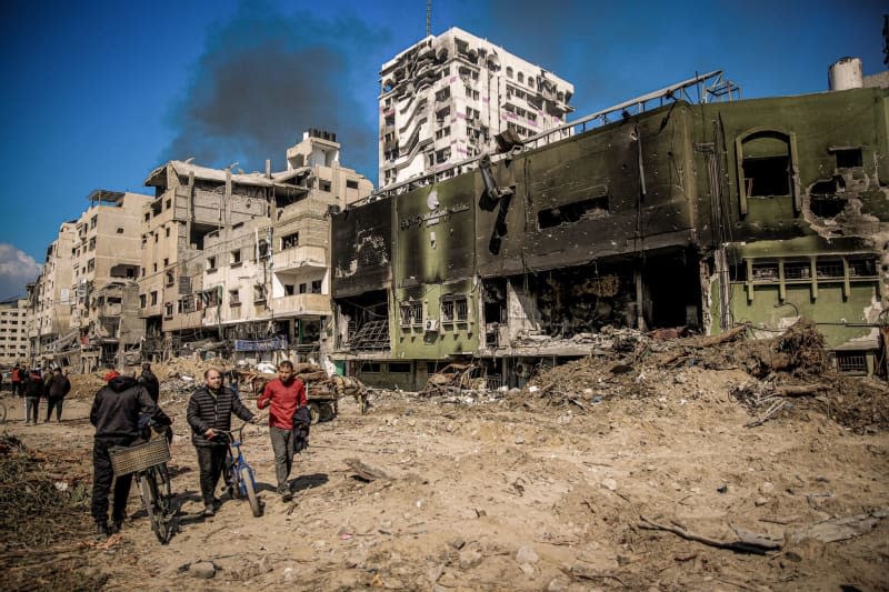 Palestinians walk next to damaged buildings on their way back to their homes in the wake of the Israeli army withdrew from North of Gaza City. Omar Ishaq/dpa