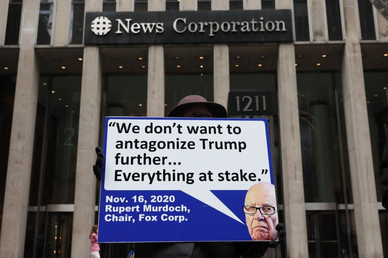 A protestor stands outside the News Corp headquarters in New York carrying a sign with an image of Rupert Murdoch and a speech bubble that reads: "We don't want to antagonize Trump further... Everything at stake." Below is the date Nov. 16, 2020.