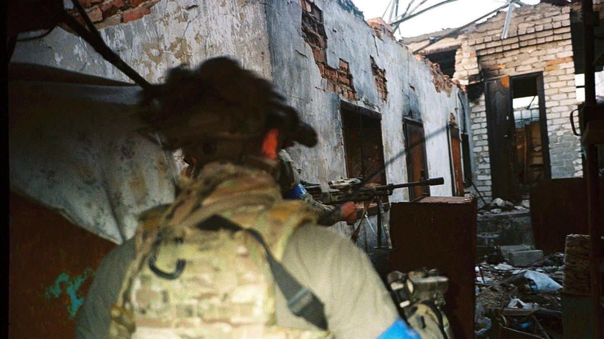 Two untrained and armed Ukrainian soldiers stand in front of a heavily bombed building