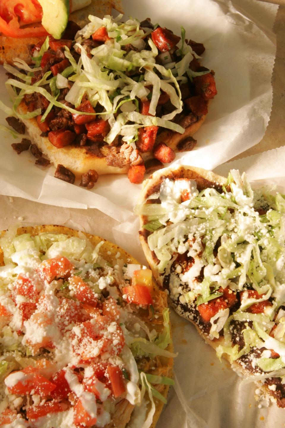 A sampling from La Lupita Tacos Mexicanos. At top is a Mexican torta with chorizo, fried pork, and steak. At bottom left is a chicken tostada, and at right is a huarache with chorizo and steak.