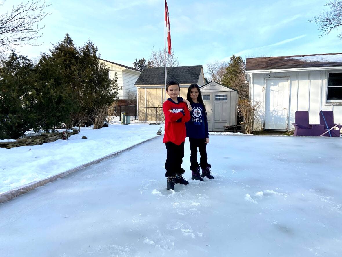 Jaxon and Alexandra Borromeo, 10-year-old twins, stand on their slushy backyard rink in London, Ont., on Wednesday. The changing climate has some people wondering about the fate of outdoor rinks.  (Submitted by Stephanie Borromeo - image credit)