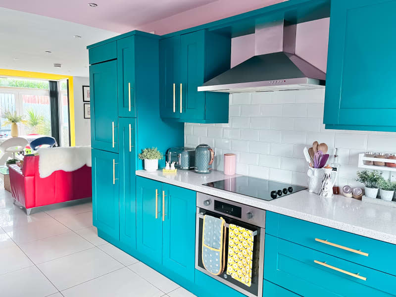 Kitchen after renovation/painting. Bright turquoise cabinets and drawers, pink ceiling, white counters, white subway tile backsplash, bright brass/gold hardware, yellow and pink accents