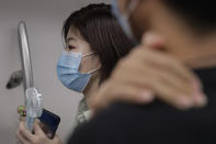 A woman wearing a face mask to protect against the new coronavirus uses an electric fan to cool herself as she rides in a subway train in Beijing, Wednesday, July 29, 2020. China reported more than 100 new cases of COVID-19 on Wednesday as the country continues to battle an outbreak in Xinjiang. (AP Photo/Andy Wong)