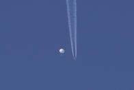 In this photo provided by Brian Branch, a large balloon drifts above the Kingstown, N.C. area, with an airplane and its contrail seen below it. The United States says it is a Chinese spy balloon moving east over America at an altitude of about 60,000 feet (18,600 meters), but China insists the balloon is just an errant civilian airshipused mainly for meteorological research that went off course due to winds and has only limited “self-steering” capabilities. (Brian Branch via AP)