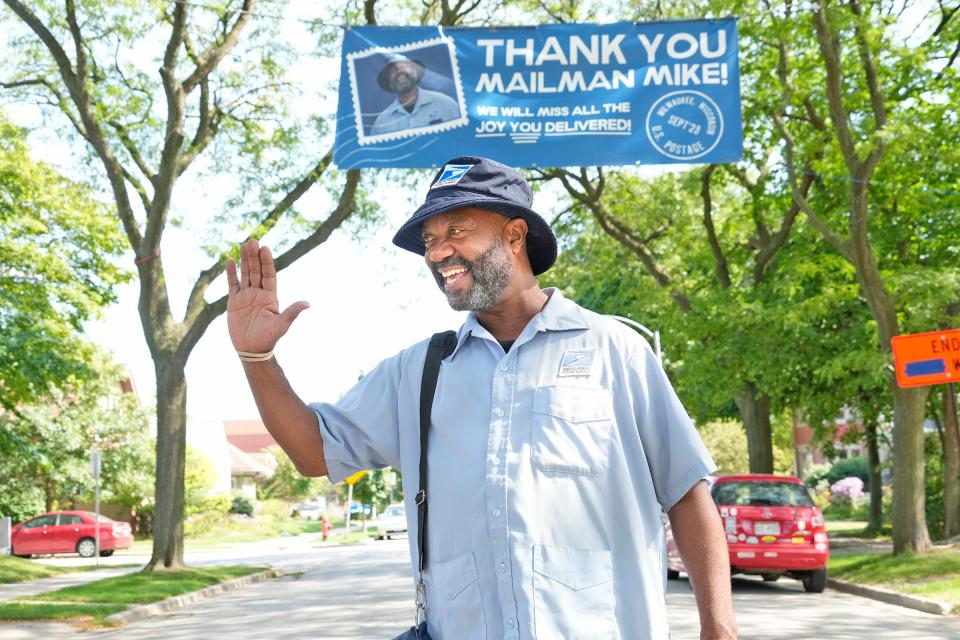 United States Postal Services carrier, Michael Boothe known as “Mailman Mike” in the Riverwest neighborhood, stands under a banner hoisted in his honor along his route near the corner of East Burleigh Street and North Dousman Street in Milwaukee on Friday. Boothe is retiring Saturday after delivering mail along the same route for 30 years.