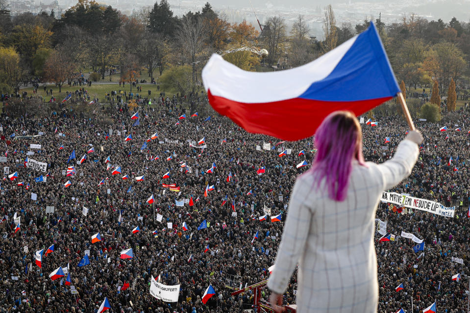 A woman waves a Czech flag from a roof as people take part in a large anti-government protest in Prague, Czech Republic, Saturday, Nov. 16, 2019. Czechs are rallying in big numbers to use the 30th anniversary of the pro-democratic Velvet Revolution and urge Prime Minister Andrej Babis to resign as peaceful protesters from all corners of the Czech Republic are attending the second massive protest opposing Babis at Letna park, a site of massive gatherings that significantly contributed to the fall of communism in 1989. (AP Photo/Petr David Josek)