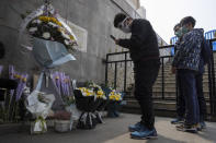 FILE - In this April 4, 2020, file photo, residents wearing masks stand in front of flowers placed near the Heroes Memorial Monument after a national moment of mourning for victims of coronavirus in Wuhan in central China's Hubei Province. A 10-member team of international researchers from the World Health Organization hopes to find clues as to the origin of the coronavirus pandemic in the central Chinese city of Wuhan where the virus was first detected in late 2019. (AP Photo/Ng Han Guan, File)