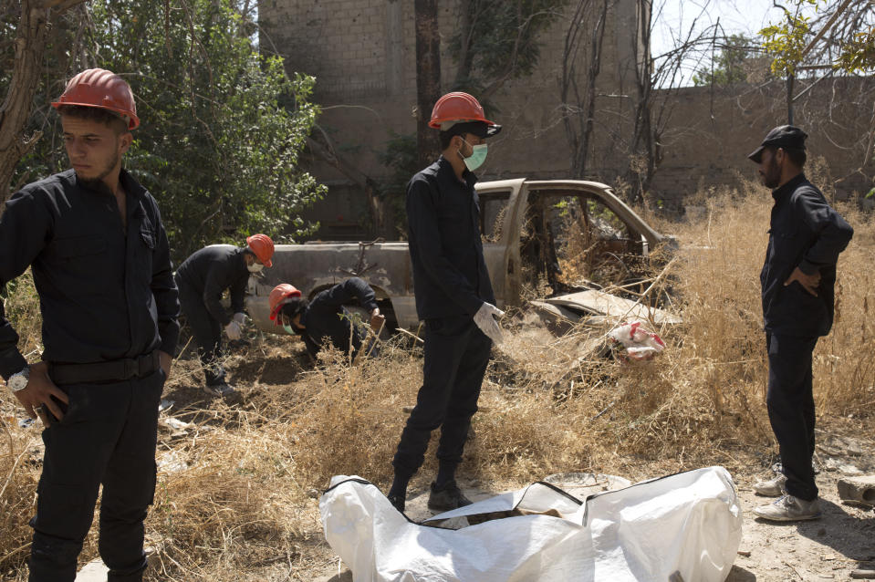 In this Saturday, Sept. 7, 2019 photo, first responders prepare to carry away a body at the site of a mass grave in Raqqa, Syria. First responders said they have pulled nearly 20 bodies out of the latest mass grave uncovered in Raqqa, the Syrian city that was the de facto capital of the Islamic State group. It is the 16th mass grave in the city, and officials are struggling with a lack of resources needed to document and one day identify the thousands of dead who have been dug out. (AP Photo/Maya Alleruzzo)