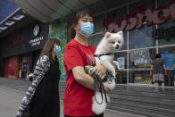 A woman wearing a mask to curb the spread of the coronavirus holds her dog as they pass by a mall in Beijing on Monday, June 29, 2020. Even as the world surpassed two sobering coronavirus milestones Sunday -- 500,000 confirmed deaths, 10 million confirmed cases -- and hit another high mark for daily new infections, China on Monday reported a further decline in new confirmed cases. (AP Photo/Ng Han Guan)